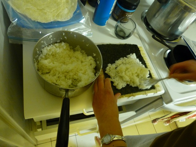 Making sushi rolls: Putting the rice onto the seaweed.