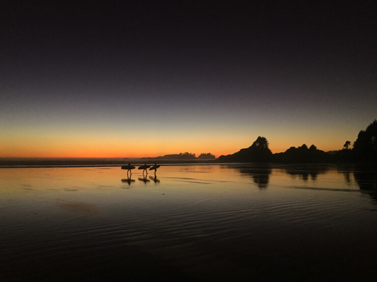 Surfers leaving the waves of the Pacific after sunset in Tofino, Vancouver Island