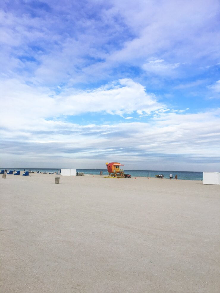 Lifeguard tower in the distance among lots of white sand in South Beach, Miami