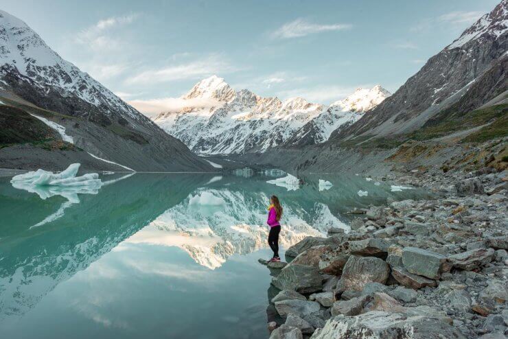 Woman staring out at the icy water in Mount Cook National Park, a bucket list destination on the South Island of New Zealand. 