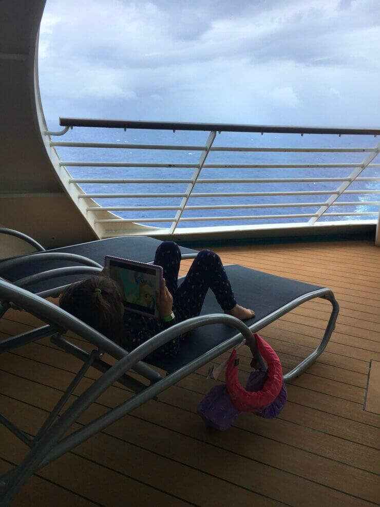 Child relaxing with a tablet on a Royal Caribbean cruise ship balcony.